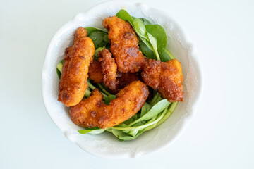 Fried chicken breast in bite-sized pieces with greens in a white bowl close-up