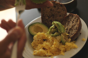 Hands Engaged in Eating Avocado and Eggs