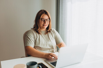 Happy cheerful cute beautiful business woman in glasses sit indoors in office using laptop...