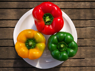 Top view of fresh tasty bell peppers on the plate on the wooden surface