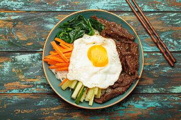 Plate of bibimbap, a mixed rice dish with meat and assorted vegetables, traditional Korean cuisine. The dish is seasoned with gochujang - chili pepper paste - and topped with a fried egg