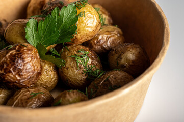 fried new potatoes cooked with golden skin, fast food delivery in kraft paper packaging on light background, place for inscription