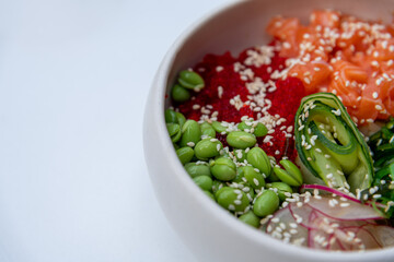 Close-up view of seafood poke bowl with salmon, rice, cucumber, radish, nori seaweed and edamame beans on white table in restaurant or sidewalk cafe. Soft focus. Copy space. Food theme.