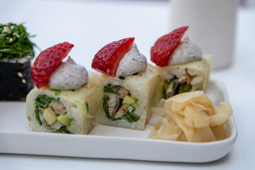 Close-up view of sushi rolls with conger eel meat and strawberry served in plate on white table in sidewalk cafe or street restaurant. Soft focus. Food theme.