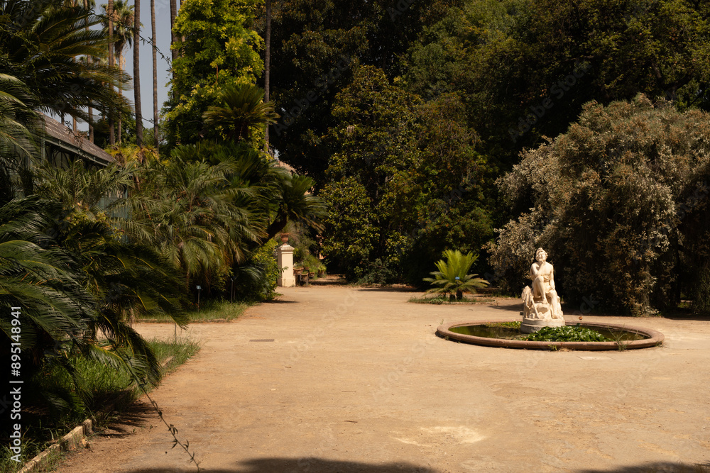 Poster a stone statue sits in the center of a circular fountain surrounded by lush greenery