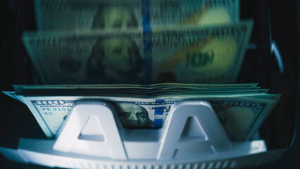 Anonymous person counts savings in hundred dollar bills for currency exchange or investment in cash counting machine. Automatic bill counter. 100 USD bank notes. Finance and banking concept. Close Up.