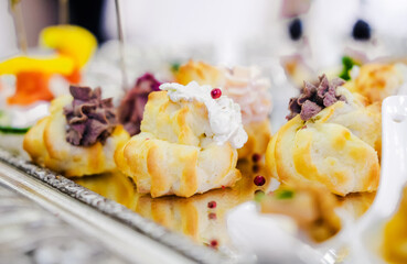 Assorted Savory Pastries with Creamy Fillings. Close-up of assorted savory pastries topped with various creamy fillings, displayed on a reflective tray. Horizontal photo.