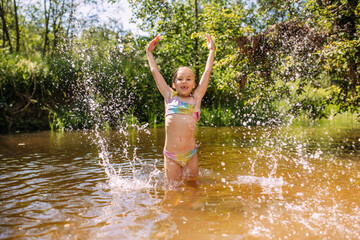 Fototapeta premium a girl child bathes in the water of the river laughter joy splashes summer heat