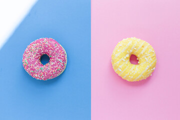 Two delicious sweet donuts lie on a colored background. Pink donut on a blue background and a delta donut on a pink background. Flour sweets. Tasty and Yummy. Unhealthy food