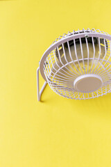 Creative mini fan stands and blows on a yellow background. Heat and air conditioning