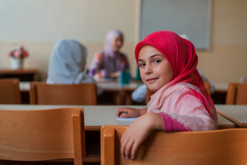 Happy Muslim girl sitting at school desk during the class in the classroom. 