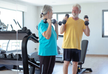 Smiling and active senior couple doing exercises with dumbells in gym area. Sport, health, gym, wellness concept