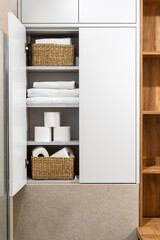 White cabinet with fresh bath towels and toilet paper rolls in wicker baskets