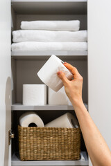 Hand reaching for toilet paper in a bathroom cabinet