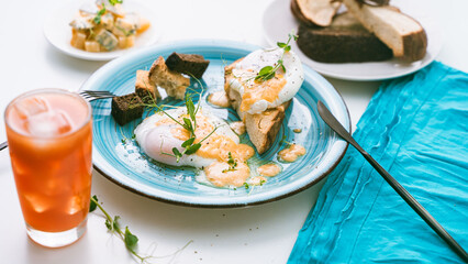 Summer healthy and delicious breakfast: eggs Benedict on toast with pea greens on a blue plate with orange or grapefruit juice and cutlery. selected focus. Close-up, top view.