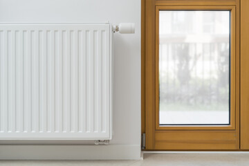 Radiator is mounted on a white wall next to a window