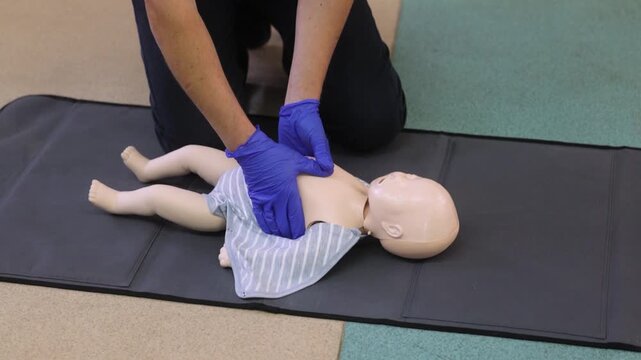 Person performing CPR on an infant dummy, focusing on chest compressions. Man Teaching First Aid, Close-Up of Dummy - Powered by Adobe