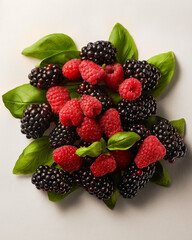 Blackberries, raspberries and green basil leaves on white