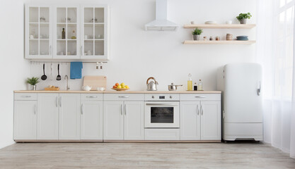 White scandinavian kitchen interior with dining room and wooden floor. Simply furniture with utensils, shelves with crockery and plants in pot, refrigerator in modern minimal design, empty space