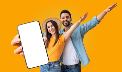 Obraz premium Multiracial couple stands together in front of a bright yellow background. The woman is holding a smartphone with a blank screen