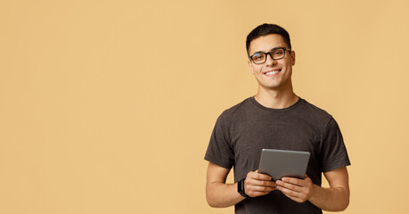 Teacher, tutor, blogger or student. Cheerful young attractive man in glasses looks at camera, holds digital tablet on online lesson, isolated on light background, panorama, empty space, studio shot