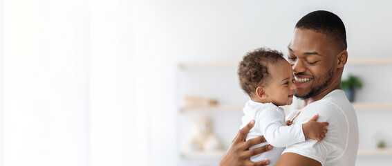 Child Care. Portrait Of Happy African American Father With Infant Baby In Arms Standing Near Window...