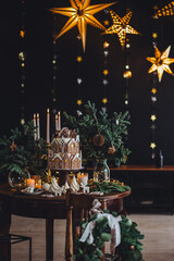 Family holiday celebration. Beautiful traditional homemade gingerbread house. Celebration of Christmas and Happy new year at home. Festive mood, cozy atmosphere, burning candles, fir tree branches