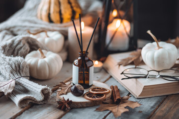 Home comfort, coziness, aromatherapy. Cozy fall interior with knitted wool warm sweater, burning candles and autumn aroma perfume diffuser. Pumpkin pie scent, maple sirup, cinnamon, anise, dry citrus