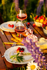Perfect surprise date for loving couple, private wedding, romantic marriage proposal. Summer, sunset, golden hour. Appetisers. Beautiful elegant outdoor arrangement in meadow with purple blue lupins
