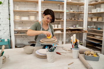 Ceramics workshop. Applying more moisture on clay products. Smoothing clay with a sponge. Using...