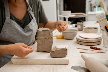 Slicing off a chunk of clay from a large block using a sharp wire clay cutter. Using a wire cutter to cut off a piece of clay before modeling the product.