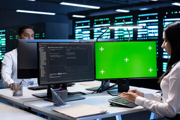 Naklejka premium Colleagues working on green screen desktop PC in data center housing storage infrastructure. Coworkers using mockup computer display in server hub workspace filled with networking tech