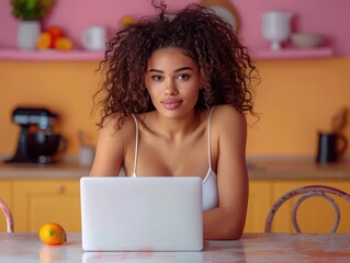 Obraz premium A woman with curly hair uses a laptop in a bright, modern kitchen with pastel-colored walls, plants, and other kitchen items in the background.