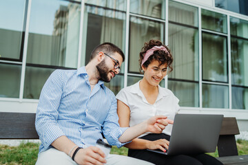 Two smiling business people working on laptop in front modern business building