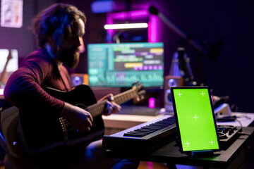 Singer producer playing acoustic guitar looking at daw software interface to record new tunes,...