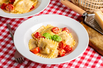 Creamy Italian Ravioli with tomatoes. Table with traditional red and white chess tablecloth.