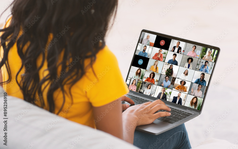 Poster black woman with long, black hair sits on a couch while participating in an online meeting, using a 