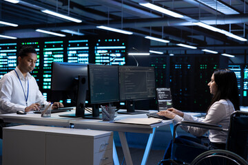 Person with disability and coworker in inclusive server room facility ensuring data remains shielded from threats. Wheelchair user and colleague protecting data center hardware equipment