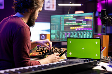 Audio engineer pushing pre amp knobs on mixing console in home studio, using laptop with greenscreen display. Music composer editing soundtracks, stereo instrument on daw software.