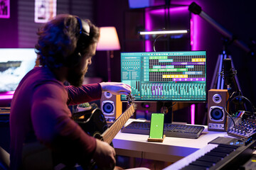 Beginner artist learning strings accords to play guitar by watching tutorials and online lessons, smartphone shows greenscreen mockup. Singer practicing acoustic instrument skills in home studio.