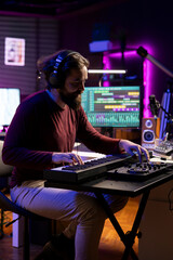 Songwriter plays midi controller piano notes in his home studio, using daw software on computer to record audio files. Young musician playing tunes on electronic keyboard, post production.