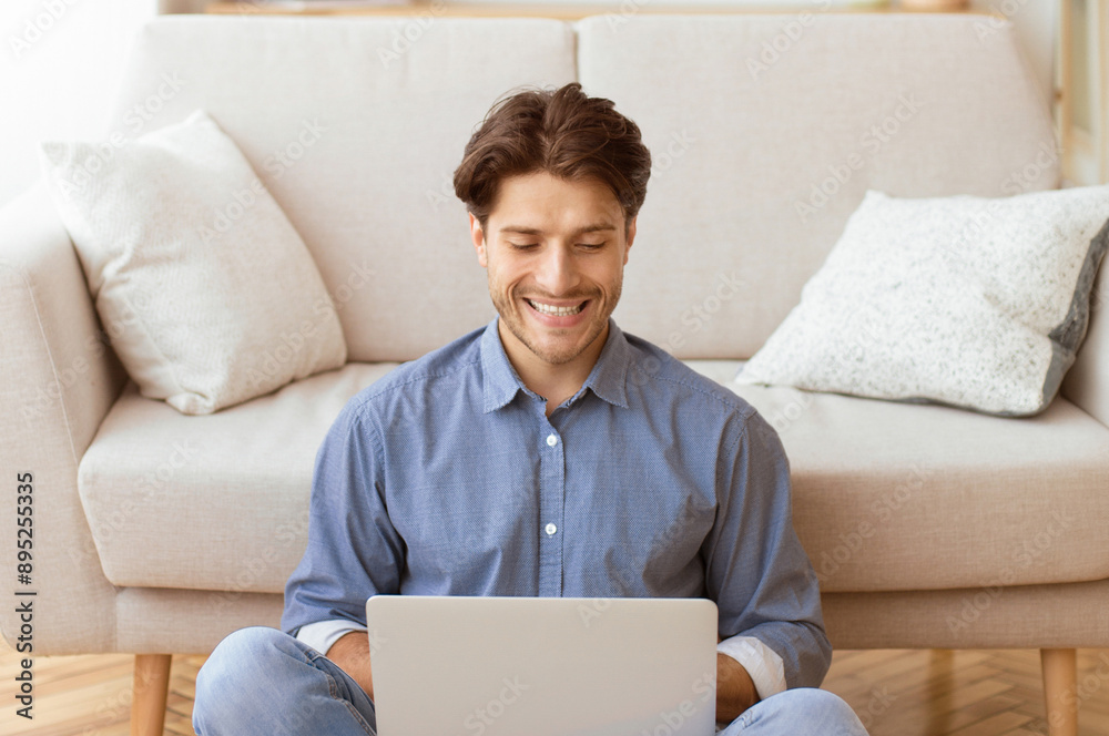 Aufkleber a man sits on the floor in front of a couch, smiling as he uses a laptop.