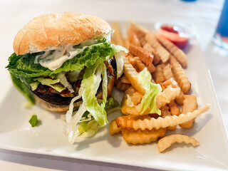 Portobello mushroom burger with fries on a white square plate and a white tablecloth 