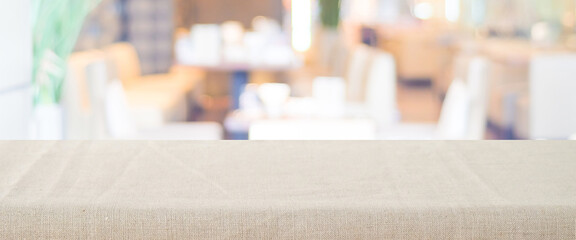 Empty table with linen tablecloth over blurred restaurant, cafe with bokeh background banner, food and product display montage