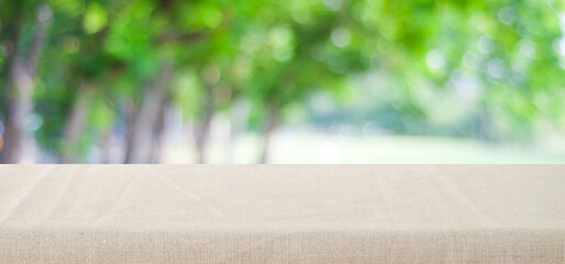 Empty table with brown linen tablecloth over blurred park nature background, for product display montage, spring and summer