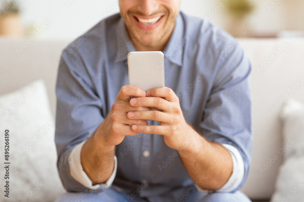 Poster happy man texting at phone. guy playing on smartphone sitting on sofa at home