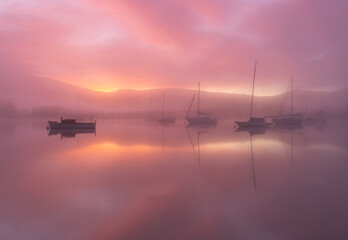 Misty morning in the bay with yachts and sailing boats in very calm waters. Sunrise mist with an orange/red/pink hue in the sky