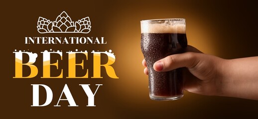 Hand holding glass of dark beer on yellow background. Banner for International Beer Day