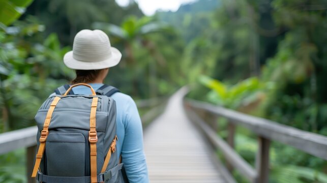 A solitary traveler with a large backpack walks along a wooden bridge in a lush green jungle setting under a bright sky, suggesting adventure and exploration. - Powered by Adobe