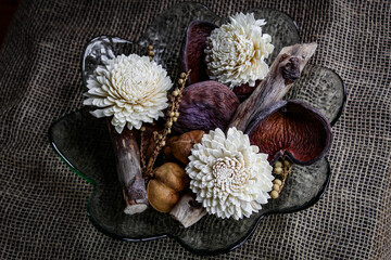 Deocrative dried flowers, seed pods, and branches in glass bowl on burlap